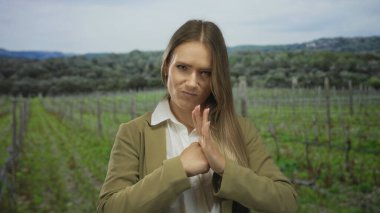 Sarışın genç bir kadın, açık bir parkta avucunun içine yumruk tokuşturarak arka planda doğal yeşillik ve eğlence ifadeleri sergiliyor..