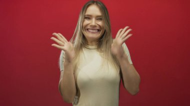 Sarı saçlı, neşeli tavırlı, izole edilmiş kırmızı arka planda heyecanını ifade eden bir kadın stüdyo ortamında canlı duygular ve pozitif enerji sergiliyor..
