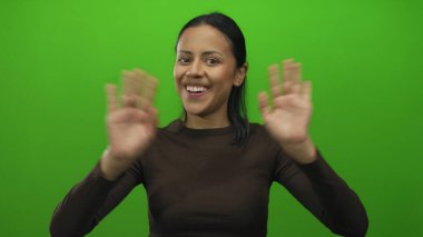 İzole edilmiş yeşil arka plan duvarına gülümseyen genç bir kadın, neşe ve pozitifliği ifade ediyor, çeşitli yaratıcı ve profesyonel projeler için uygun..