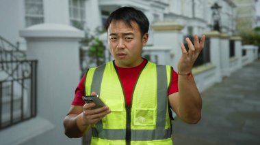 Sarı yelek giyen bir adam, şehir caddesinde akıllı telefon kullanarak modern şehir yaşamını ve teknoloji kullanımını gözler önüne seriyor..