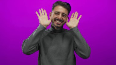 Gri balıkçı yakalı genç adam gülümseyen bir balıkçı yaka Stüdyoda açık avuçlarla el kaldırır;.