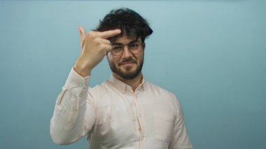 Sakallı ve gözlüklü genç adam mavi arka planda kaba bir hareket gösteriyor..