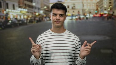 Genç adam hareketli şehir caddesinde sıradan çizgili gömleğiyle, canlı şehir gece lambalarıyla çevrili duruyor.