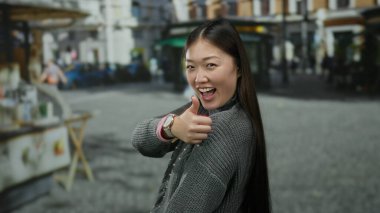 Gülümseyen bir kadın, Çin 'de bir şehir caddesinde gri bir kazak giyip uzun saçlarını gösterirken başparmağını kaldırıyor..