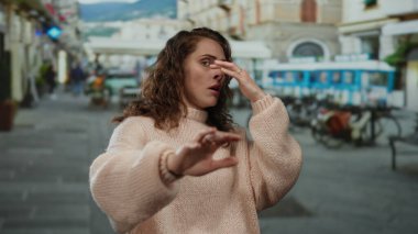 Şehrin arka planında parlayan güneş ışığı ya da beklenmedik bir olayı gösteren şehir manzarasından rahatsız olmuş gibi görünüyor..