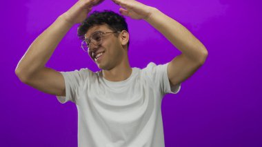 Gülümseyen adam mor stüdyoda çatı jesti oluşturmak için kollarını kaldırır; sevinç kutlaması yaratıcılığı.