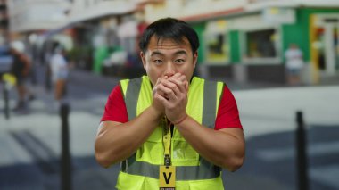 Yansıtıcı yelek giyen genç adam kalabalık bir şehir sokağında şaşkınlığını dile getiriyor..