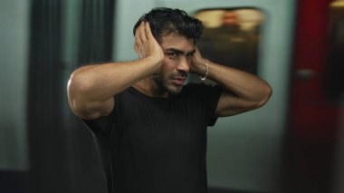İspanyol genç adam, yoğun istasyon binasında hareket halindeki trenin yanındaki platformda iki eliyle kulaklarını kapatıyor..
