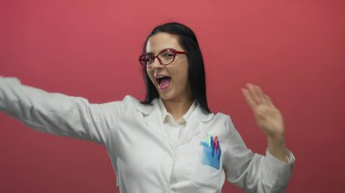 Canlı kırmızı arkaplan karşısında laboratuvar üniformasıyla kutlama yapan kadın, bilimsel başarıyı ve neşeli enerjiyi eğlenceli ve dinamik bir ortamda sembolize eder..