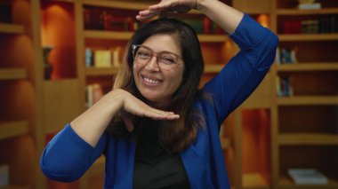 Mavi hırkalı kadın elleri ve kitaplığın önünde gülümseme ile yüzünü çerçeveler; yaratıcı vizyon sevinç.