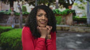 Orman yolunda çene altına yumruk atan, yeşil çalılar ve yosunlu taşlarla kaplanmış kırmızı bluzlu bir kadın..