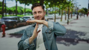 Sakallı genç adam güneşli bir şehir caddesinde mola veriyor..