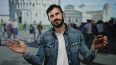 Sakallı İspanyol adam sidik kulesinin yanında duruyor, kot giyiyor, hareketli bir İtalyan kasabasının arka planında..