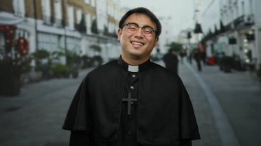 Dini giyinmiş gülümseyen bir adam gözlüklü ve haçlı bir bornoz takmış bir şehir merkezinde kültürel ve ruhsal bir tema öneriyor..