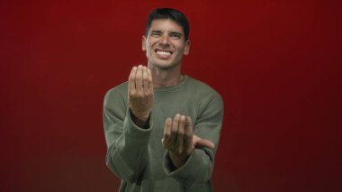 Süveter giyen İspanyol adam geniş bir gülümseme ile elleri ile işaret kırmızı arka plan;.