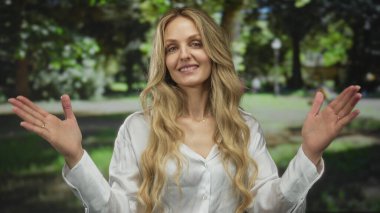 Güneşli bir park ortamında neşeli bir şekilde gülümseyen kadın, yemyeşil ağaçlarla çevrili, huzurlu bir açık havada mutluluk ve sükunet yayıyor..