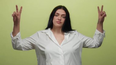 İzole edilmiş sarı arkaplan önünde güven içinde el kol hareketi yapan genç bir kadın kıvrımlı, büyük beden ve beden pozitifliğini gündelik bir ortamda vurguluyor..