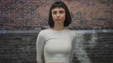 Genç İspanyol kadın başını eğiyor ve tuğla bir duvarın önünde gülümsüyor..