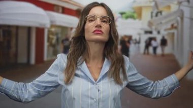 Kalabalık bir sokakta elleri olan, gözlüklü, çizgili tişörtlü, ağzı açık konuşan, şakacı konuşan bir kadın..