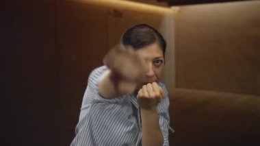 Stüdyoda tahta duvara karşı yükselen yumruklu İspanyol kadın, odaklanmış ifade ile orta jest; kararlılık.