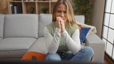 Oturma odasında kanepede otururken acı dolu bir ifadeyle el ele tutuşan kadın, diş ağrısı sıkıntısı..