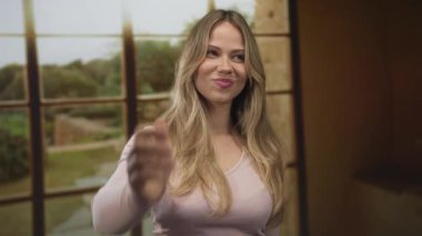 Güneşli bir oturma odasında elini uzatıp el sıkışan sarışın kadın; dostluğu hoş karşılayan bağlantı sıcaklığı.