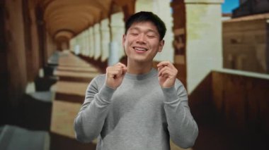 Eski üniversite koridorunda sırıtan genç bir adam, kemerleriyle güneşli gökyüzünün altında mutluluk ve eğlence taşıyor..