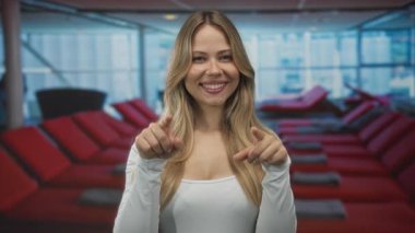 Sarışın kadın beyaz bluzlu tekne güvertesinde kamerayı işaret ediyor..