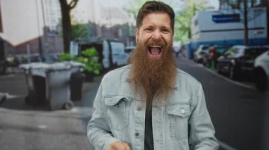 Uzun sakallı bir adam park halindeki arabaların yanındaki kalabalık bir caddede yumruklarını sıkar ve yüksek sesle bağırır; heyecan.