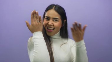 Nişanı mor arka planda kutlayan kadın elinde nişan yüzüğüyle heyecan ve neşe gösteriyor..