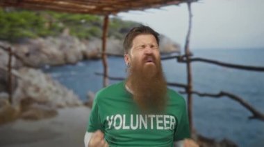 Yeşil gönüllü tişörtü giyen uzun sakallı adam, Rocky Beach 'te tahta pergola altında sıkılmış yumruğunu kaldırdı. Zafer..