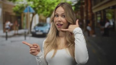 Kadın sarışın el, telefon çağrısı işareti yapıyor ve meşgul şehir caddesini işaret ediyor; iletişim bağlantısı.