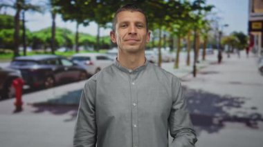 Güneşli bir günde, arka planda ağaçlar ve arabalarla elleriniz göğsünüzde gülümseyerek sokakta dikilen bir adam..