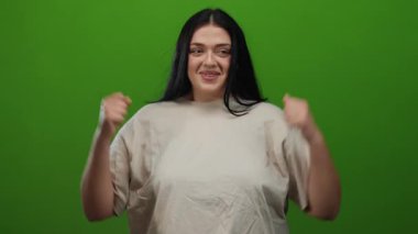 İzole edilmiş yeşil arka planda güvenle gülümseyen bir kadın günlük bej giysiler giyiyor neşeli, anlamlı bir jest, somut bir pozitiflik ve kendine güvenle.