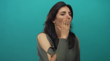 Latin kökenli orta yaşlı, siyah saçlı bir kadın avuçlanmış eline bağırıyor ve bir deniz mavisi atölyesinde çıplak kolunu açıkta bırakıyor..