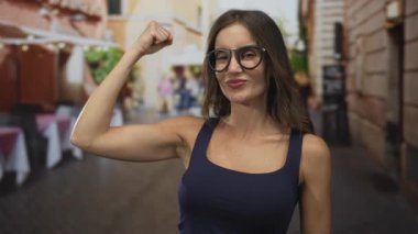 Latin kökenli gözlüklü genç bir kadın, güneş ışığı altında sokak restoranının terasında kolunda çıplak koluyla esnedi..