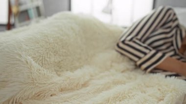 Yatak odasında yumuşak battaniyenin altında yumuşak sabah ışığında çizgili pijama giyen genç bir kadın..