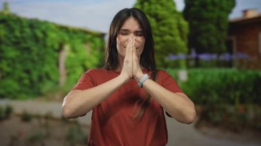 Serin bir park ortamında meditasyon yapan bir kadın, yemyeşil ağaçlar ve canlı yeşilliklerle çevrili, dua ederek sükunetini ifade ediyor..