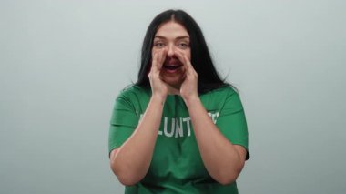 Genç ve iri yarı bir kadın, beyaz bir duvara karşı elleri ağızla bağırıyor. Coşku ve toplum ruhunu sergiliyor..