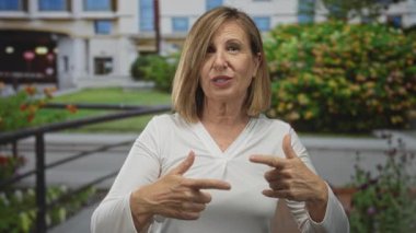 Beyaz kadın, inşaat girişinin yanındaki sakin şehir sokağında iki elini de havaya kaldırdı; belirsizlik.