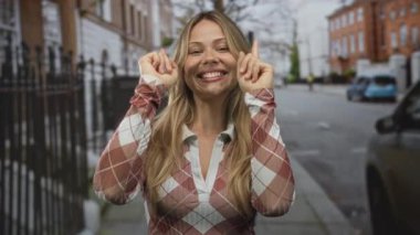 Sarışın kadın şehir kaldırımında gülümseyen bir yüzle işaret ediyor, iyimser neşe..