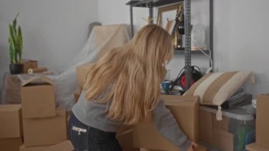 Karton kutularla çevrili yeni bir evde oturan genç bir kadın oturma odasında bavulunu açarken sırt ağrısı çekiyor..