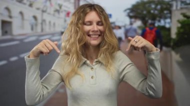 Sarışın, genç, gülümseyen kaldırım şehri kalabalığının yanında parmak tutan bir kadın..