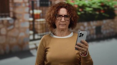 Kent sokağında taş duvar altyapısı olan akıllı telefon kullanan bir kadın orta yaşlı İspanyol kadınının gündelik yaşamında modern teknolojiyi gösteriyor..