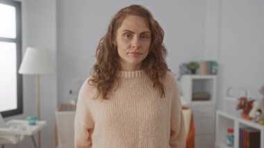 Sıcak yatak odasında bebek beşiği ile gülümseyen genç bir kadın ev ortamında sıcak bir aile atmosferi sergiliyor. İçinde bej bir kazak ve şık bir dekorasyon var..