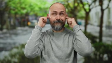 Parktaki sakallı adam kulaklarını kapatıyor. Dışarıdaki hayal kırıklığını şakasına anlatıyor..