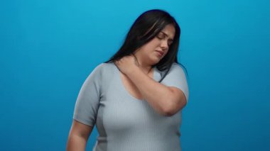 Uzun saçlı, boyuna dokunan, rahatsız hisseden, izole edilmiş mavi arka plana karşı duran, gri gömlek giyen, acıyı ifade eden, artı boyut, kıvrımlı, genç, kadın..