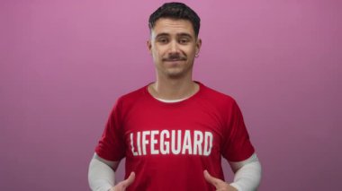 Kırmızı tişörtlü genç İspanyol cankurtaran canlı pembe bir arka plana karşı güvenle gülümsüyor, modern bağlamda güvenliği ve tarzı temsil ediyor..
