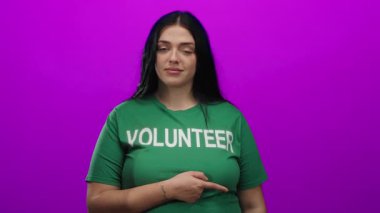 Pembe arka planda yeşil gönüllü gömlekli bir kadın kendine güvenen bir ifadeyle yanlamasına bakıyor..