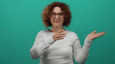 İzole edilmiş yeşil arka planı olan, elleri açık, esmer, doğrudan bakan, beyaz uzun kollu gömlek giyen, dışavurumcu jestleri vurgulayan bir kadın..